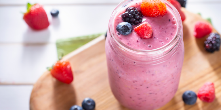 Berry smoothie in a cup surrounded by fresh raspberries and blueberries